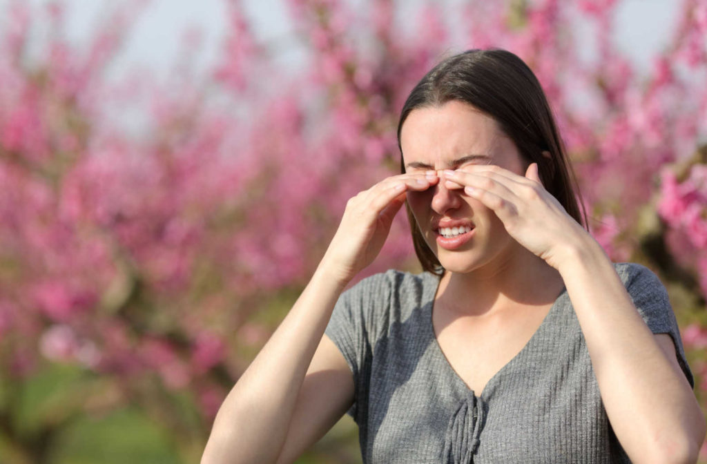 A woman outdoors is touching her itchy eyes.