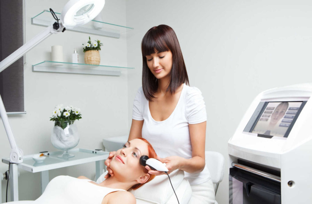An aesthetics technician applies a radiofrequency tool to a patient's face.
