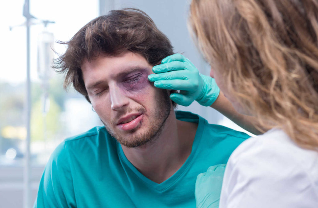 A close-up of a man with a black eye getting treatment at the hospital from a female doc. A traumatic event or injury caused to the eye can can caused floaters to the eye.