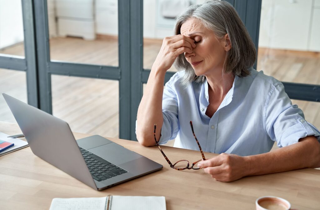 Older woman rubbing eyes while sitting at laptop.